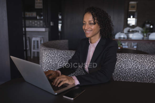 Femme d'affaires souriante assise et utilisant un ordinateur portable à la cafétéria du bureau — Photo de stock