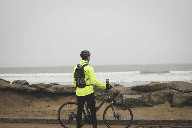 Rear view of man with cycle standing at the beach — Stock Photo