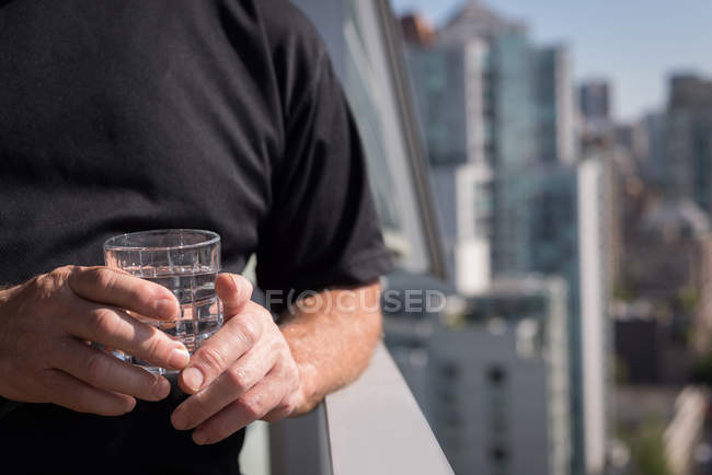 Partie médiane de l'homme tenant un verre d'eau dans le balcon — Photo de stock
