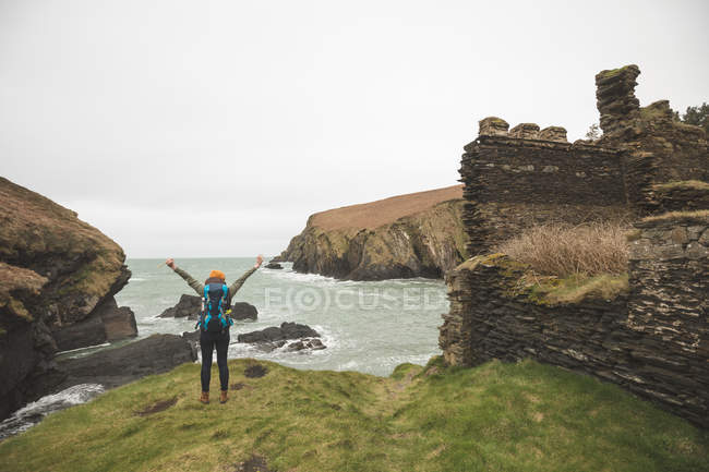 Вид сзади на женщину-туристку с распростертыми руками, стоящую на берегу моря — стоковое фото