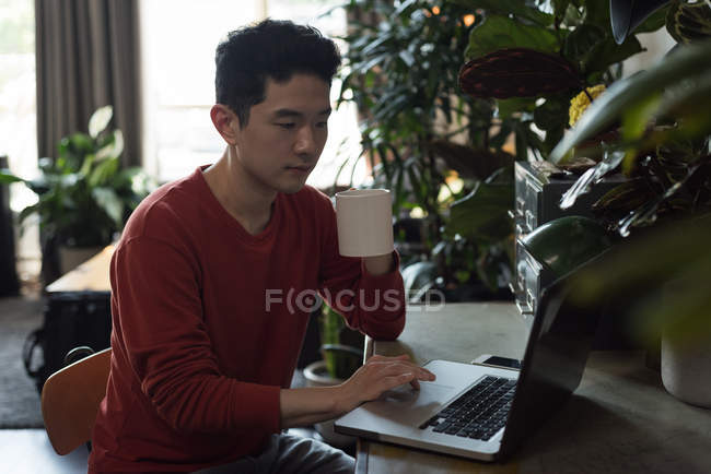Чоловік має каву, використовуючи ноутбук у вітальні вдома — стокове фото