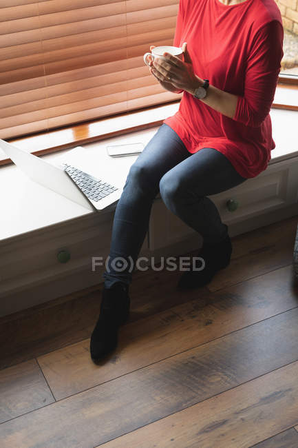 Section basse de la femme prenant un café dans le salon à la maison — Photo de stock