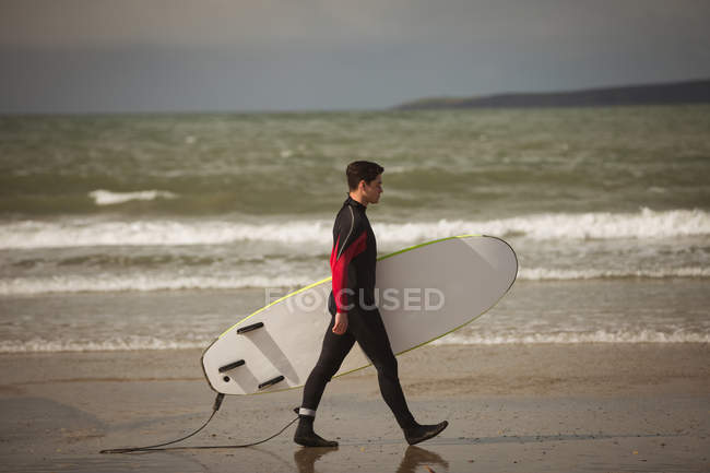 Surfeur avec planche de surf marchant sur la plage par une journée ensoleillée — Photo de stock