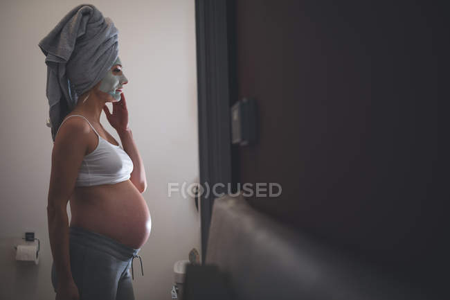 Беременная женщина с кремом для лица в ванной комнате дома — стоковое фото