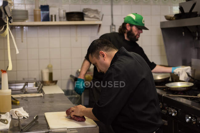 Мужчина шеф-повар режет мясо на кухне в ресторане — стоковое фото