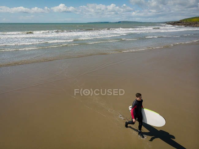 Vista de ángulo alto de Surfista con tabla de surf caminando en la playa - foto de stock