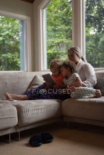 Mutter und Kinder sitzen auf dem Sofa und nutzen zu Hause das digitale Tablet — Stockfoto