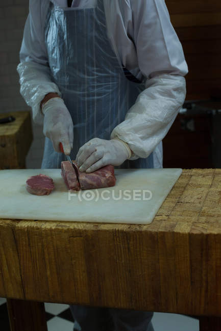 Sección media del carnicero cortando carne en la carnicería - foto de stock