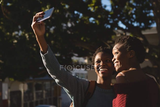 Gemelos hermanos tomando selfie con teléfono móvil en la calle de la ciudad - foto de stock