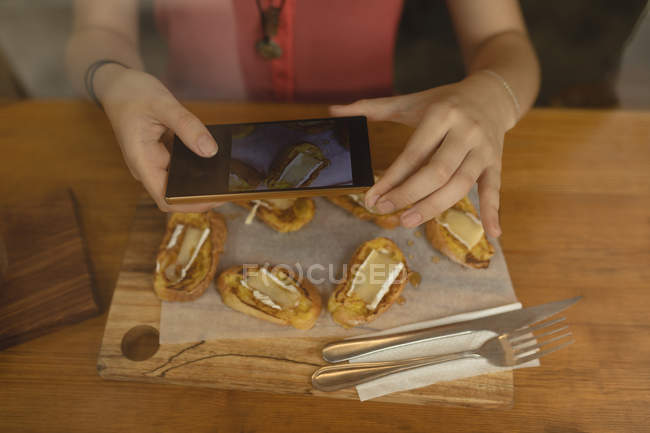 Jovem mulher fotografando comida servida na mesa em uma cafeteria — Fotografia de Stock