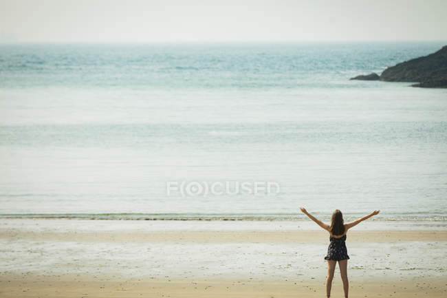 Visão traseira da mulher de pé na praia com as mãos espalhadas — Fotografia de Stock