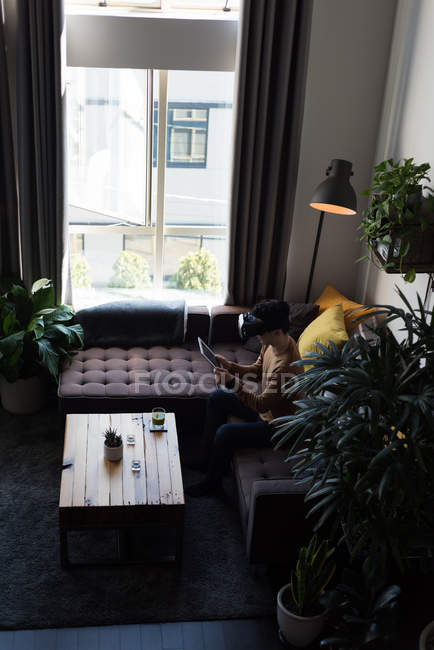Человек в гарнитуре виртуальной реальности с помощью цифрового планшета в гостиной дома — стоковое фото