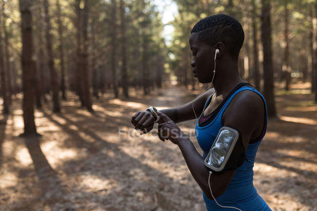Atleta hembra revisando su reloj inteligente en el bosque - foto de stock