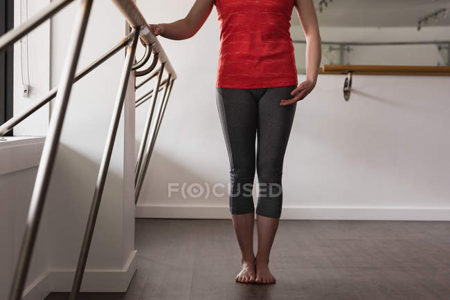 Sección baja de mujer joven de pie sosteniendo la barra en el gimnasio - foto de stock