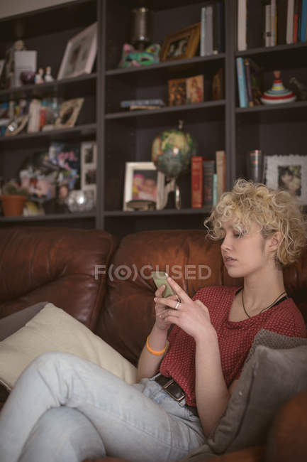 Jeune femme utilisant un téléphone portable dans le salon à la maison — Photo de stock