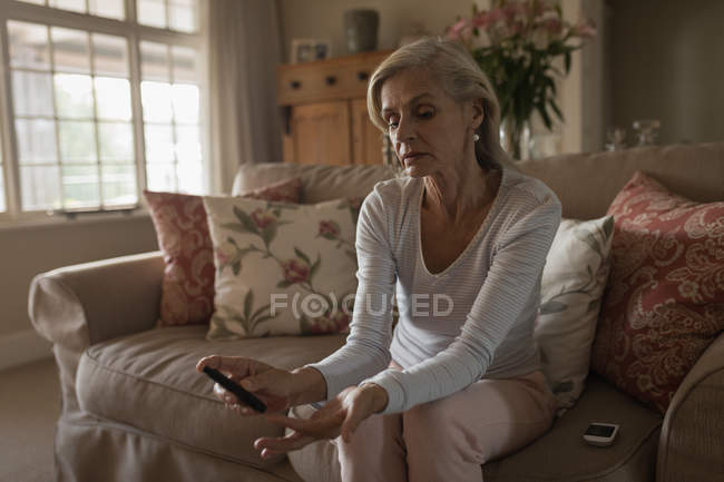 Worried senior woman with glucose meter checking blood sugar level at home — Stock Photo