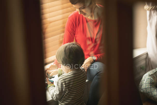 Mother playing with son on window seat in living room at home — Stock Photo