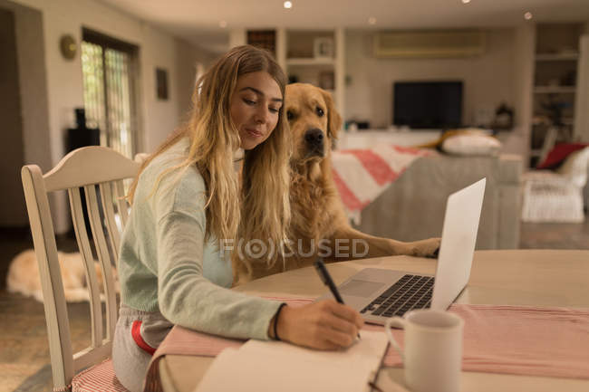 Дівчина з собакою пише на щоденнику вдома — стокове фото