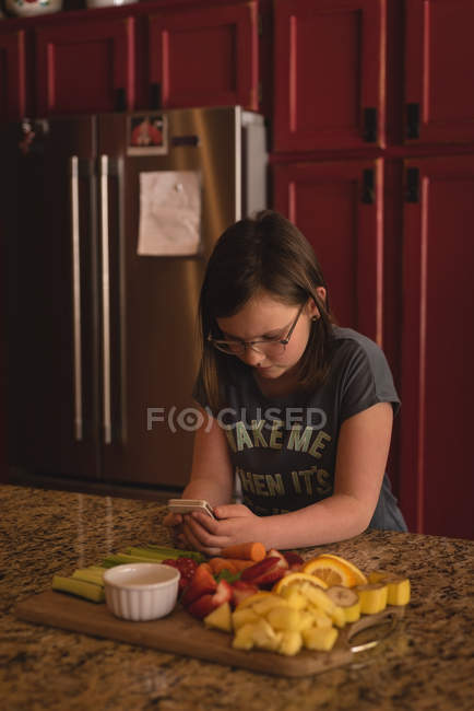Menina usando telefone celular na cozinha em casa — Fotografia de Stock