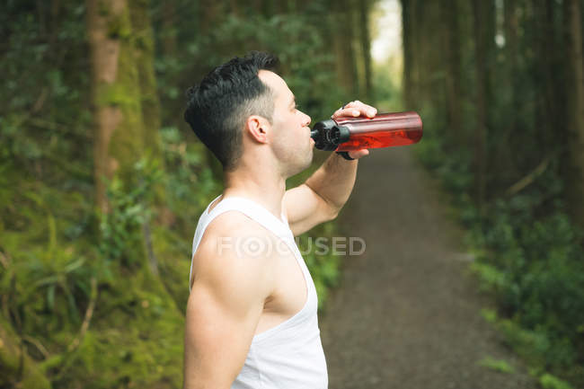 Ajuster l'homme à boire de l'eau après l'entraînement en forêt — Photo de stock
