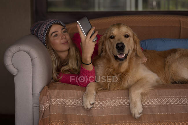 Menina com cão usando telefone celular na sala de estar em casa — Fotografia de Stock