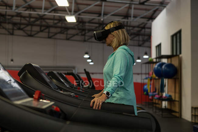 Зріла жінка використовує гарнітуру віртуальної реальності під час вправ на біговій доріжці — стокове фото
