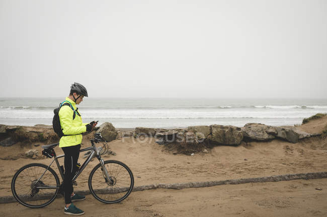Young man with cycle using mobile phone at the beach — Stock Photo