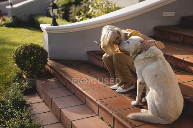 Senior woman kissing dog on the entrance steps at home — Stock Photo