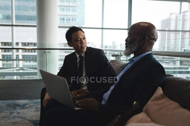 Два бизнесмена с ноутбуком обсуждают с офисом — стоковое фото