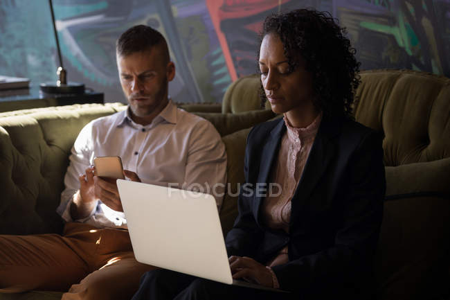 Бизнес-руководители используют ноутбук и смартфон, сидя на диване в офисе — стоковое фото