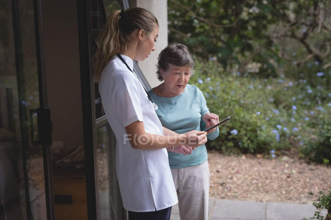 Физиотерапевт и пожилая женщина с помощью таблетки дома — стоковое фото