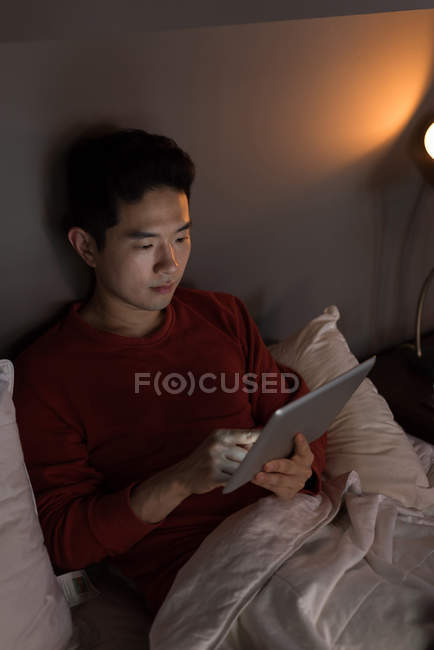Homme assis sur le lit en utilisant une tablette numérique à la maison — Photo de stock