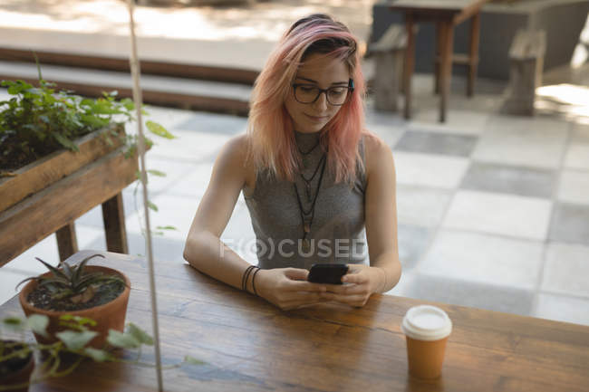 Mujer joven usando un teléfono móvil en la cafetería - foto de stock