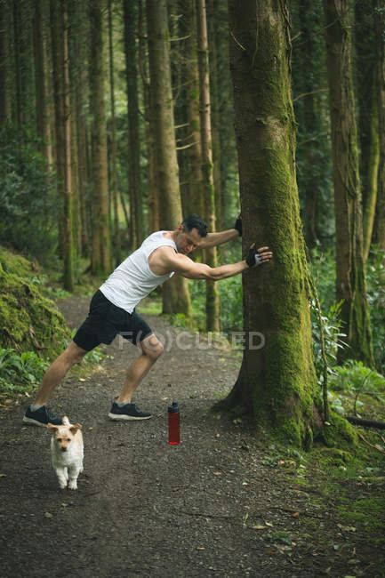 Fit man doing stretching exercise with his dog in forest — Stock Photo