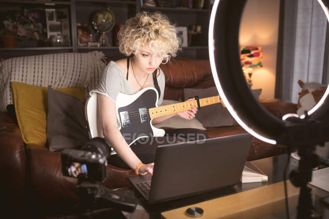 Жіночий блогер з гітарою використовує ноутбук у вітальні вдома — стокове фото