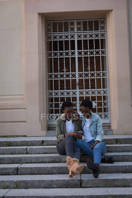 Twins siblings using mobile phone on a steps in city — Stock Photo