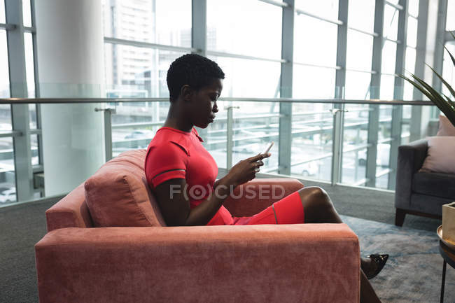 Бізнес-леді сидить на дивані і використовує мобільний телефон в офісі — стокове фото