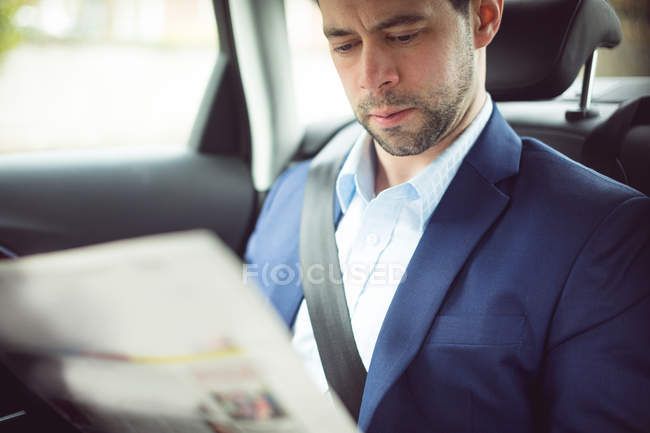 Homme d'affaires intelligent lisant un journal dans une voiture — Photo de stock