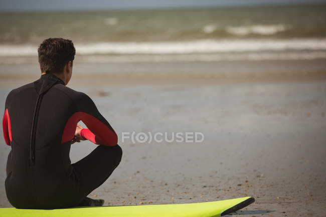 Rear view of surfer sitting on the surfboard on beach — Stock Photo