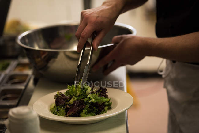 Sección media del chef masculino que sirve comida en la cocina del restaurante - foto de stock