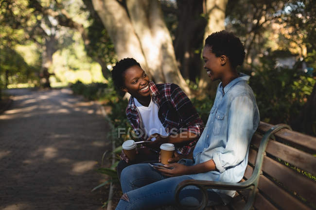 Happy twins siblings using mobile phone while relaxing on the bench — Stock Photo