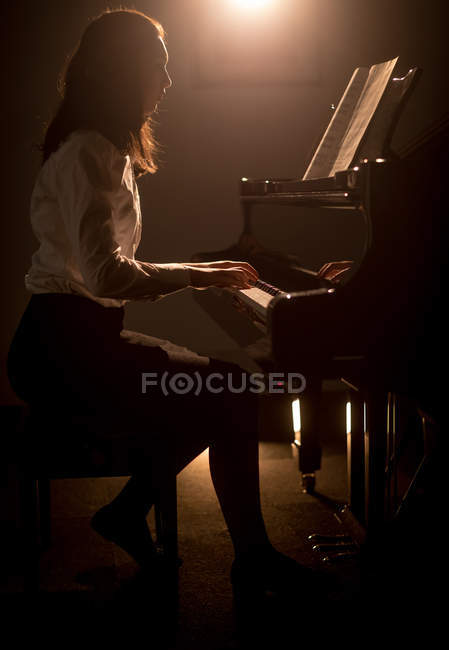 Вид сбоку на школьницу, играющую на фортепиано в музыкальной школе — стоковое фото