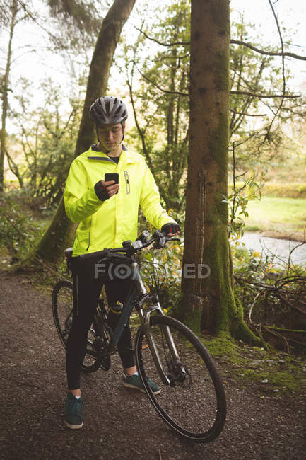 Jovem com ciclo usando telefone celular na floresta — Fotografia de Stock