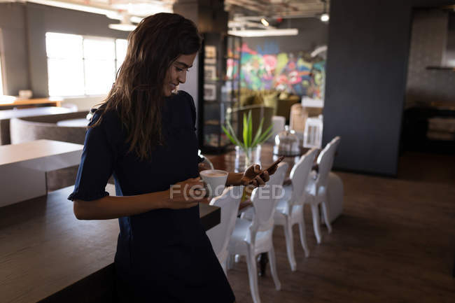 Бизнесмен, пользующаяся телефоном за чашечкой кофе в офисной столовой — стоковое фото