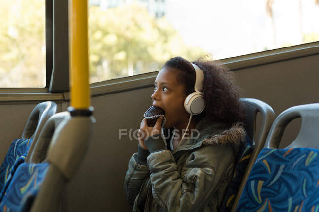 Adolescente chica teniendo cupcake mientras escucha música en los auriculares en autobús - foto de stock