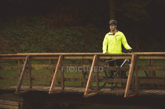 Junger Biker steht auf Holzbrücke im Wald — Stockfoto