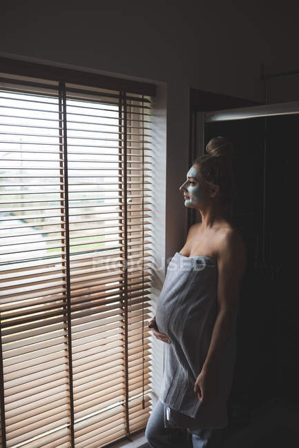 Mujer embarazada con crema facial en el baño en casa - foto de stock