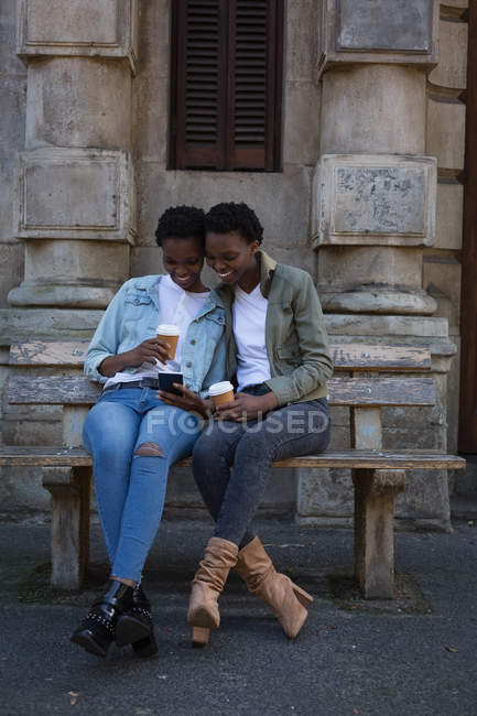 Twins siblings using mobile phone while relaxing on the bench in city — Stock Photo