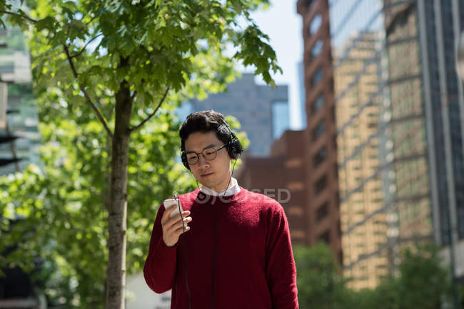 Молодой человек слушает музыку по мобильному телефону на улице — стоковое фото