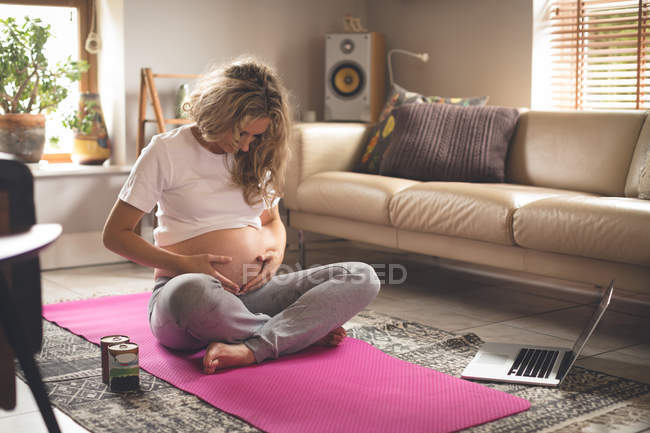 Беременная женщина прикасается к животу в гостиной дома — стоковое фото